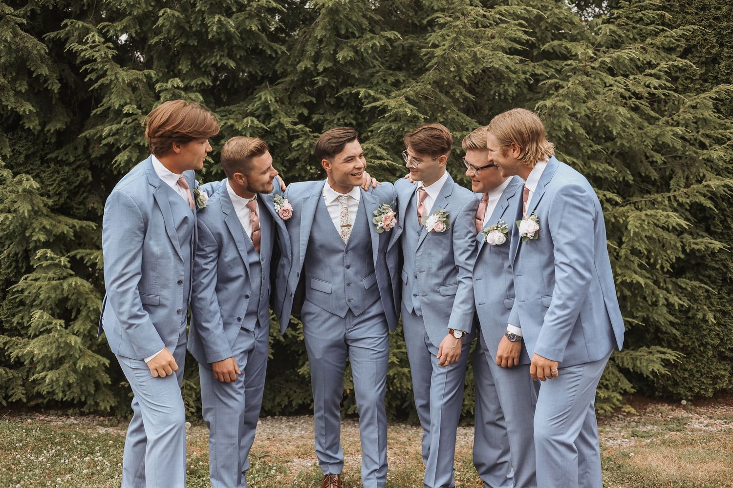 Wedding party in coordinated blue suits sharing a candid moment outdoors.