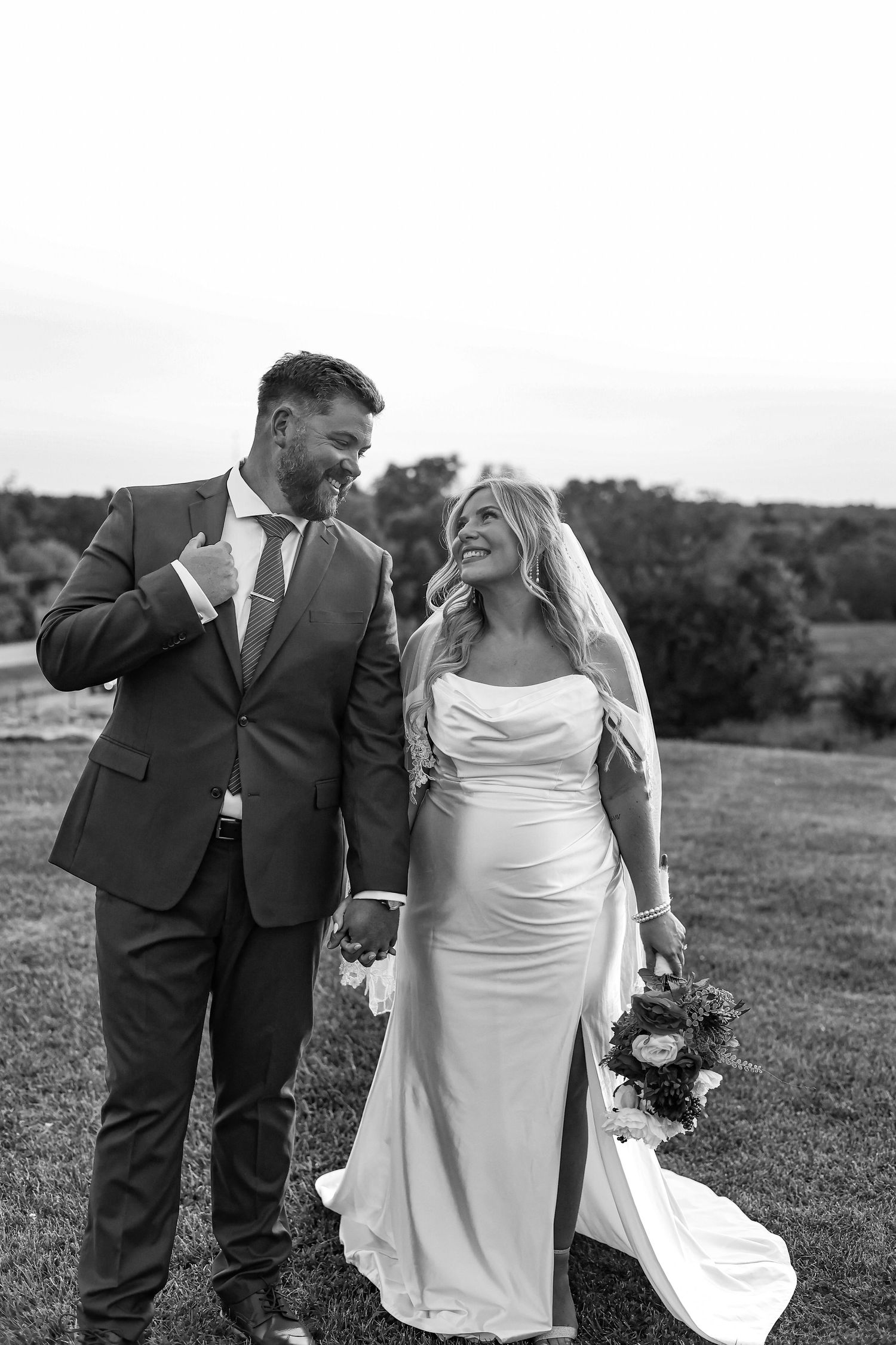 Black and white wedding photo of couple laughing together on hillside.