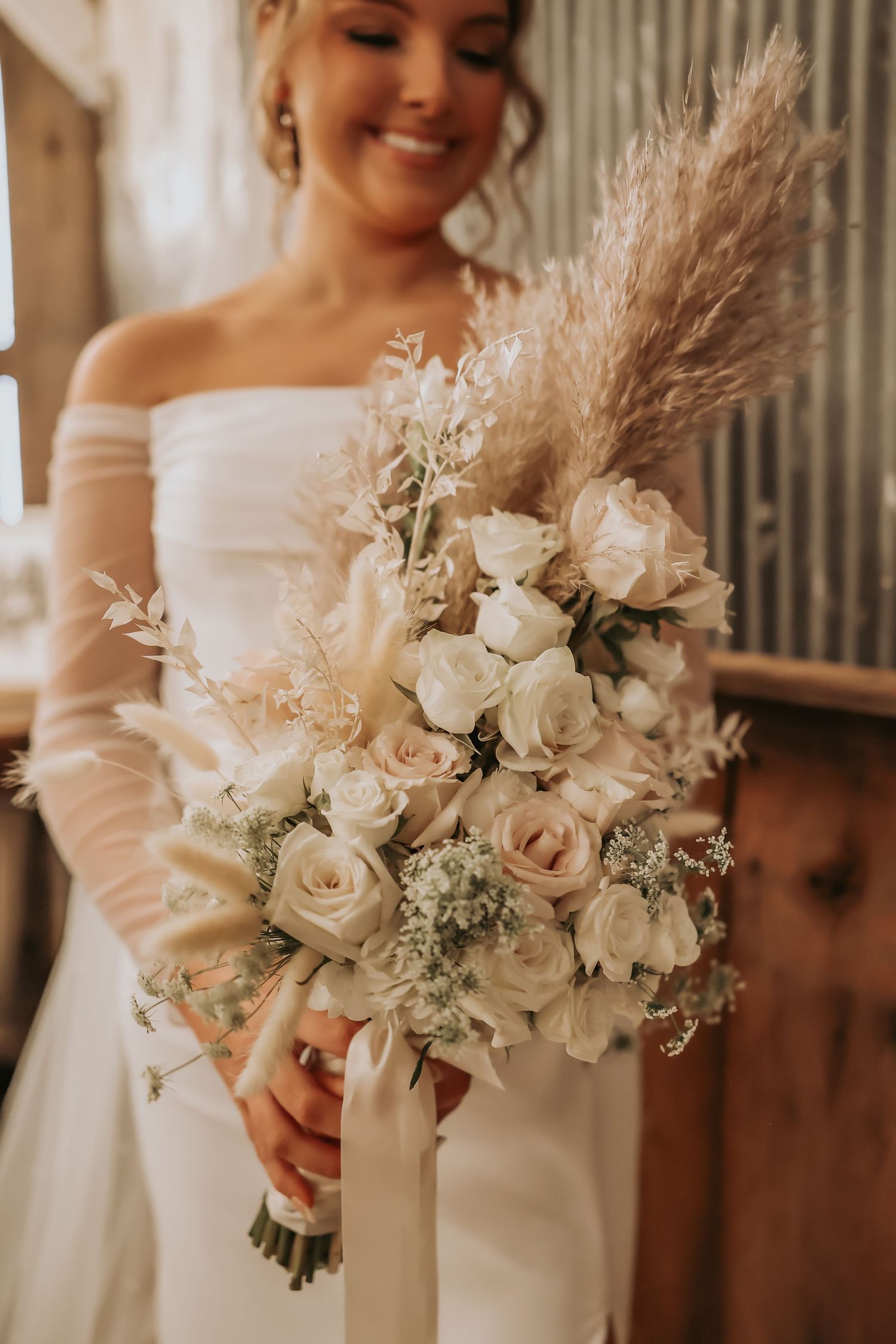 Elegant bridal bouquet featuring white roses and pampas grass in warm lighting.