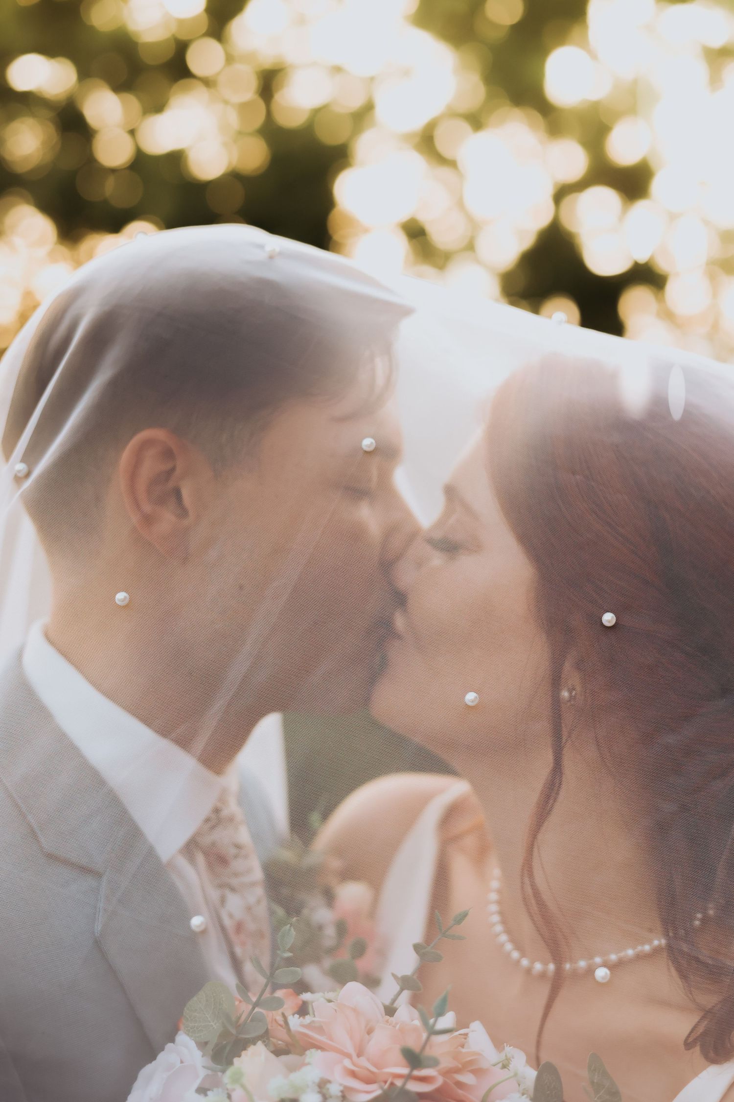 A dreamy wedding portrait through a veil with soft bokeh lighting in the background.