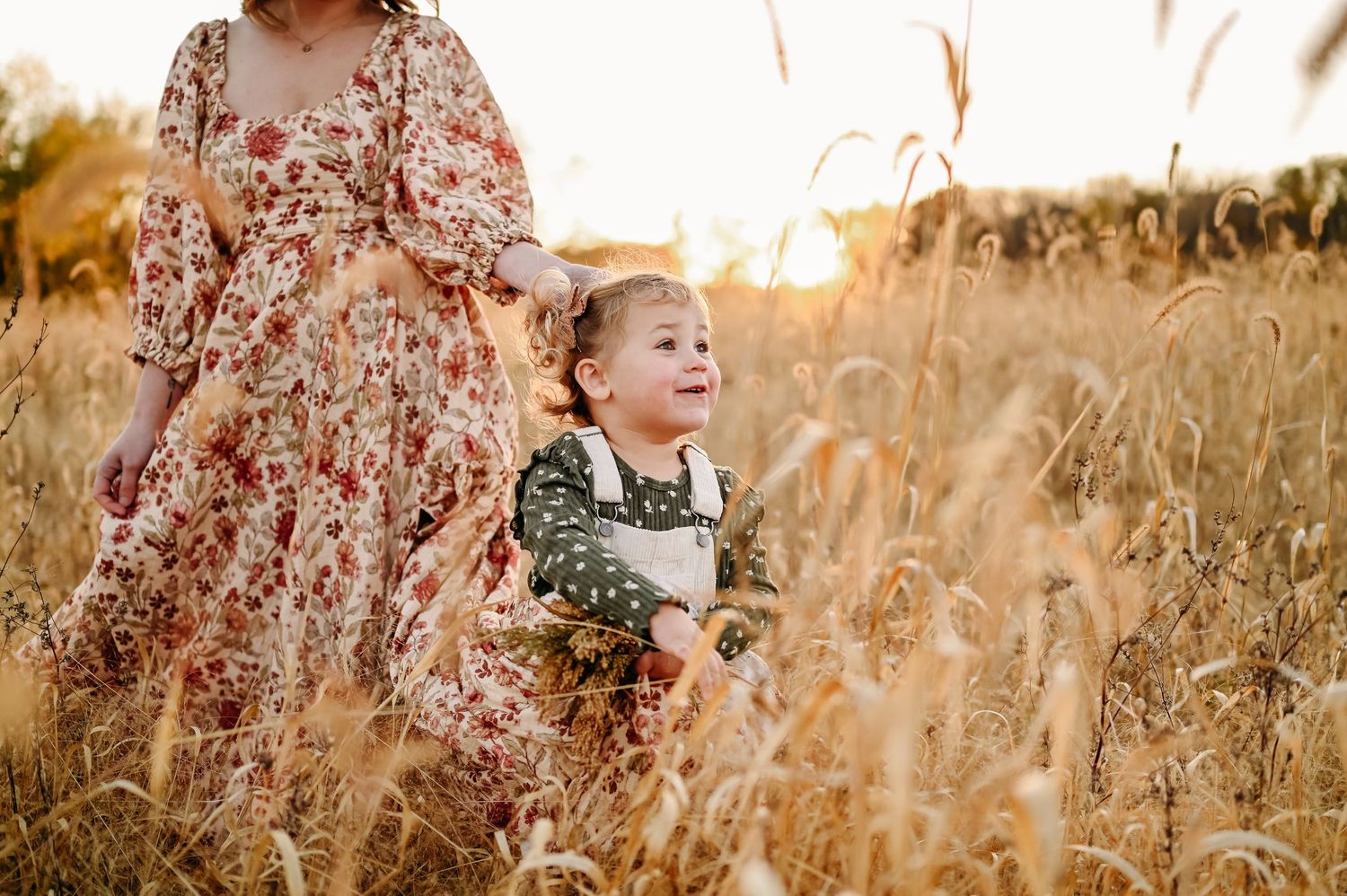 A person walks through a golden wheat field at sunset wearing a floral dress in late summer.