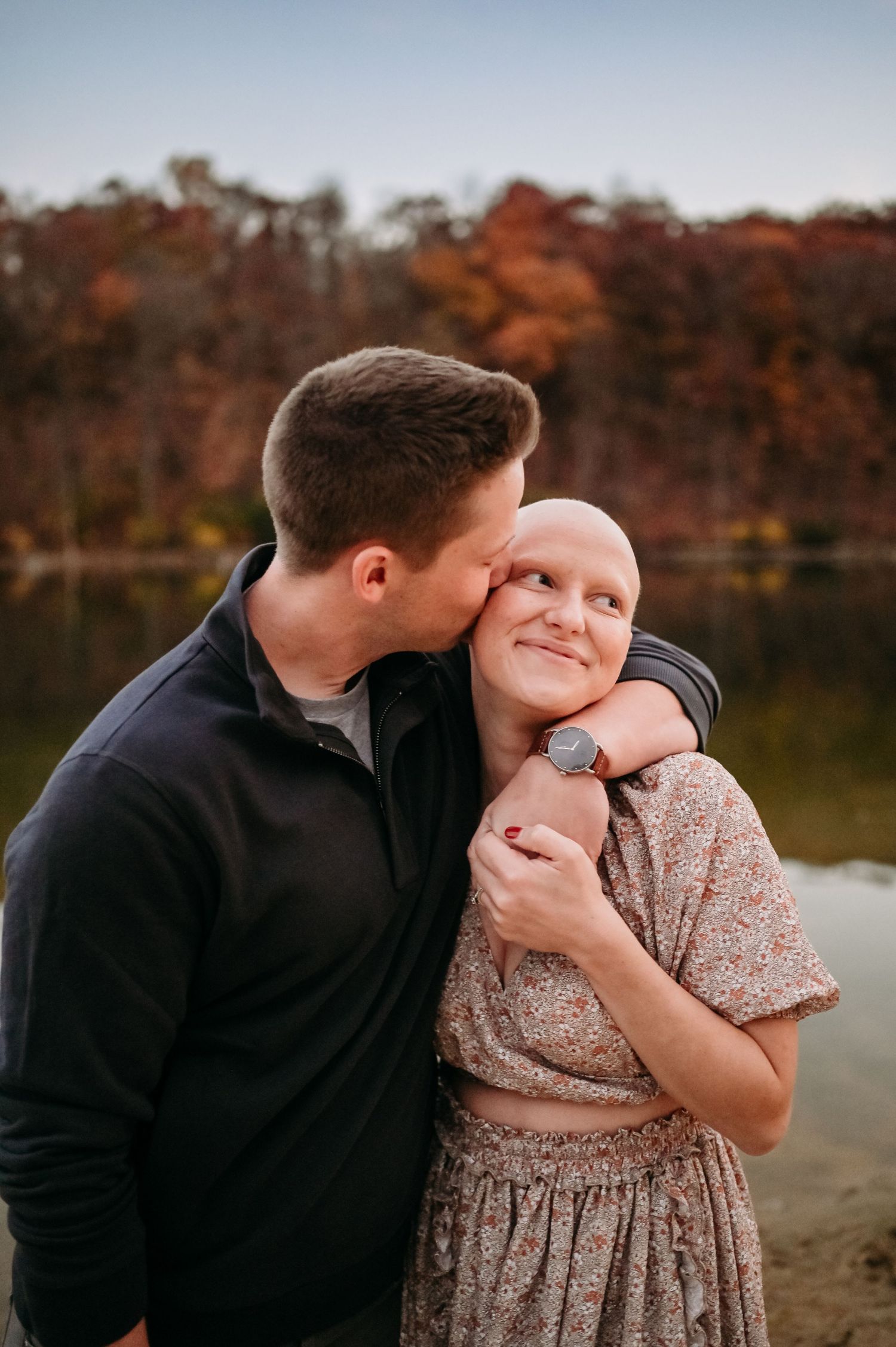 A loving embrace captured against a backdrop of fall colors and a serene lake.