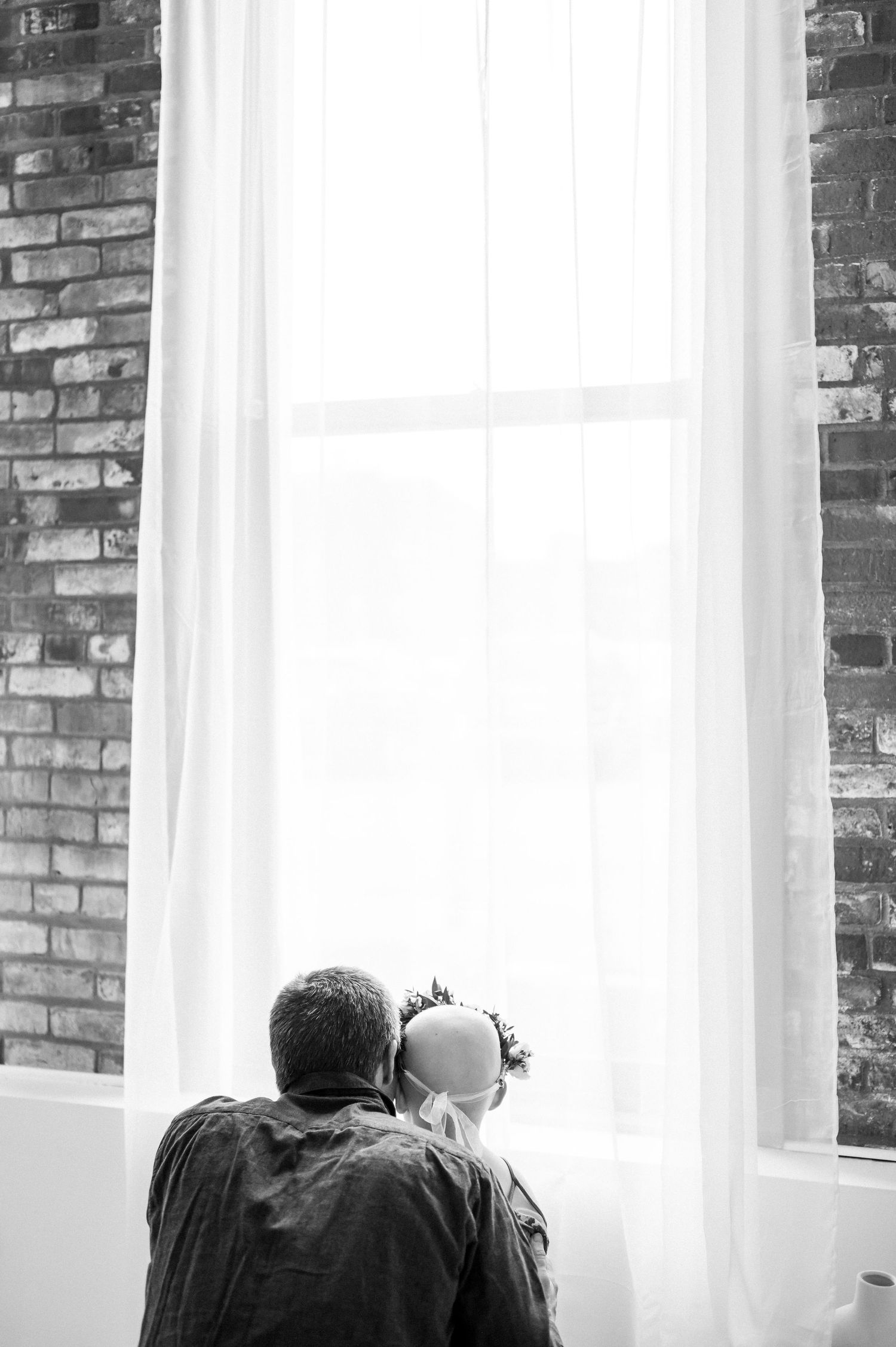 Black and white silhouette of a tender moment by a bright window with exposed brick walls.