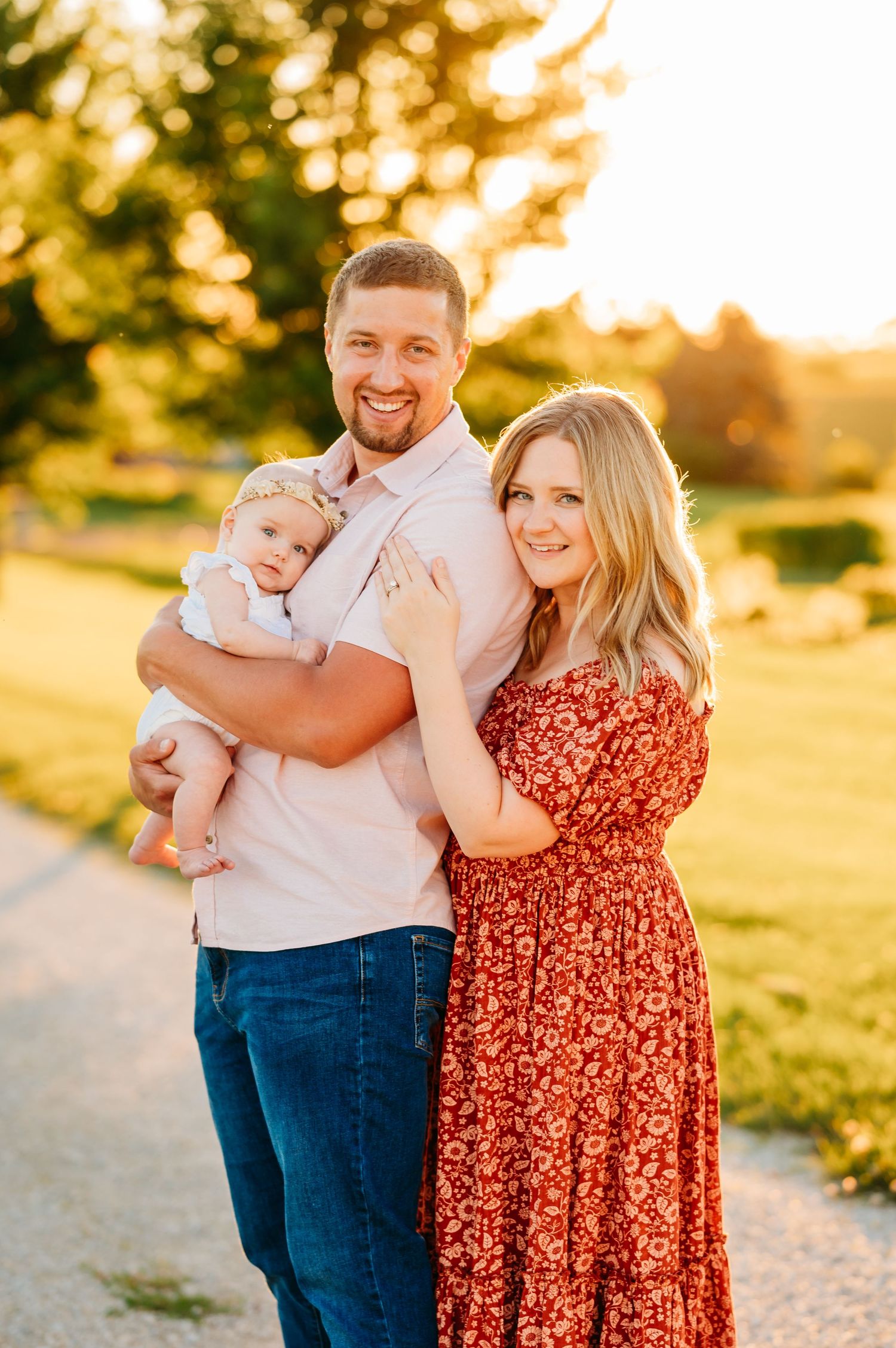 A couple enjoying golden hour photography in matching white and red clothing standing in a grassy field at sunset.