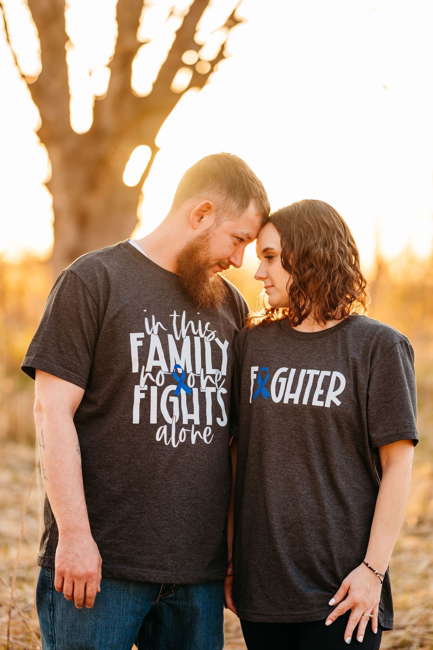 A couple wearing matching dark t-shirts embraces during golden hour in a rustic outdoor setting.