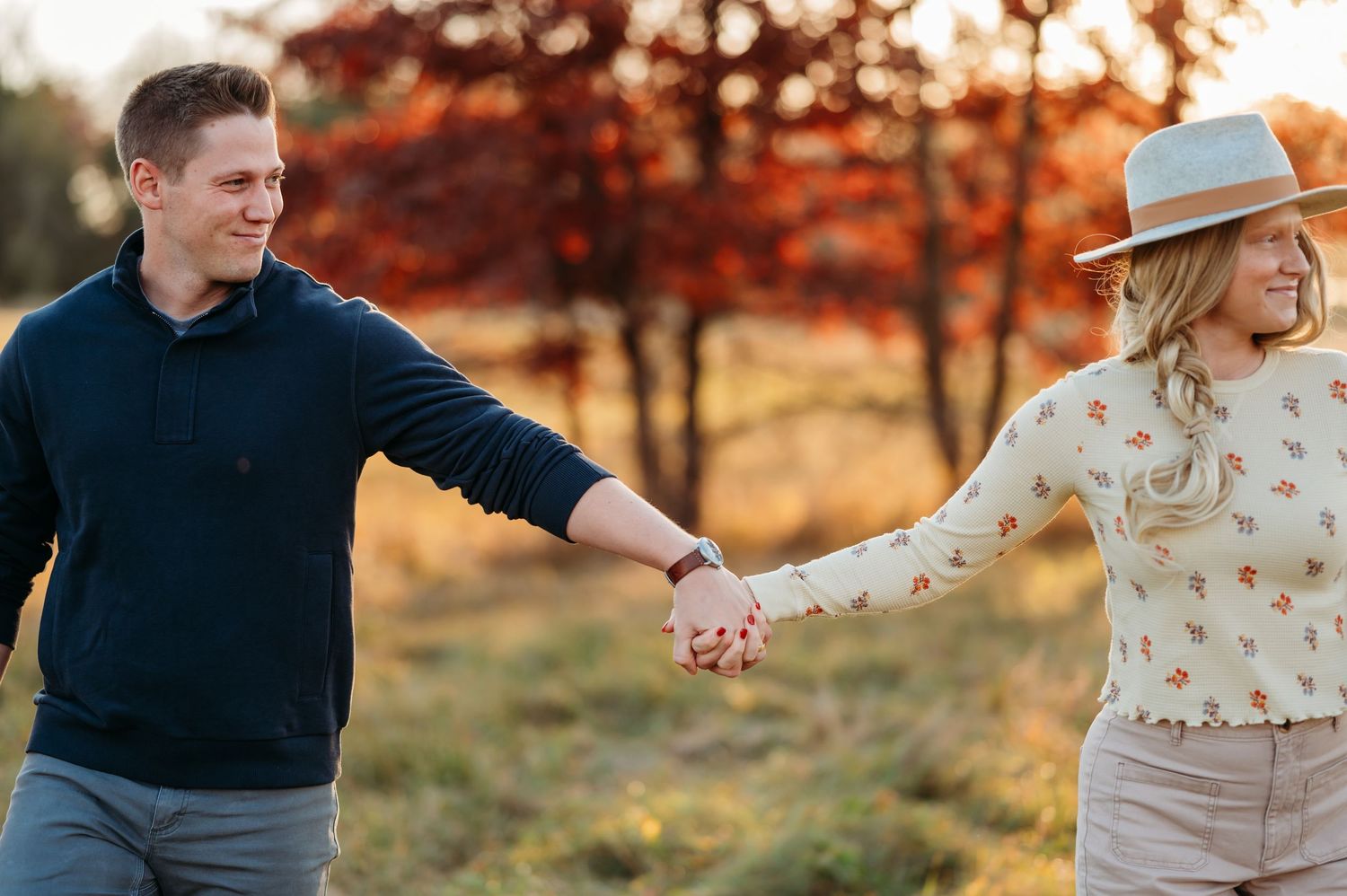 Couple walking and laughing together in a golden autumn field during sunset.