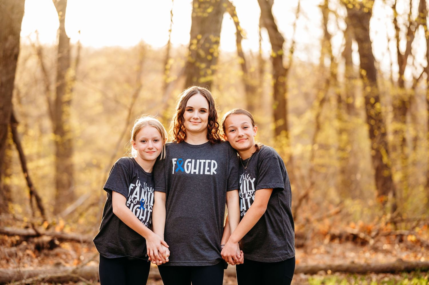 A group wearing matching black t-shirts poses together in an autumn forest setting during golden hour.