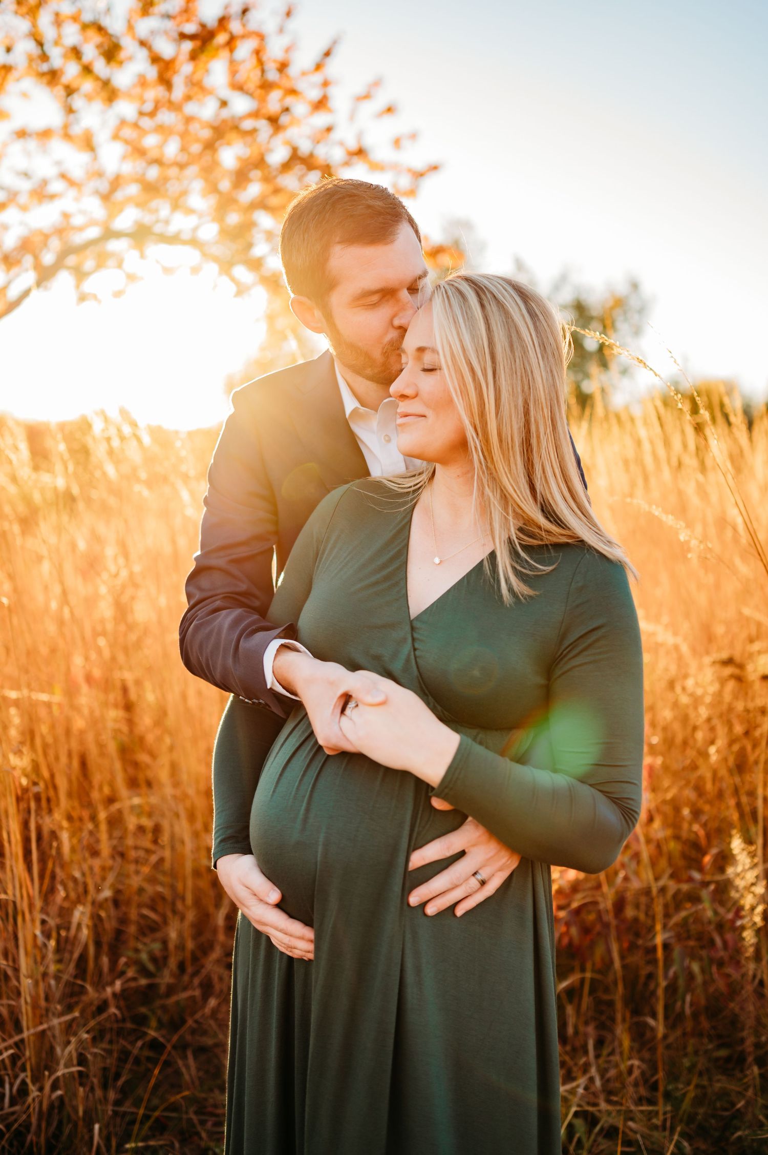 A couple embraces in a golden wheat field at sunset with glowing warm light creating a romantic maternity photo.