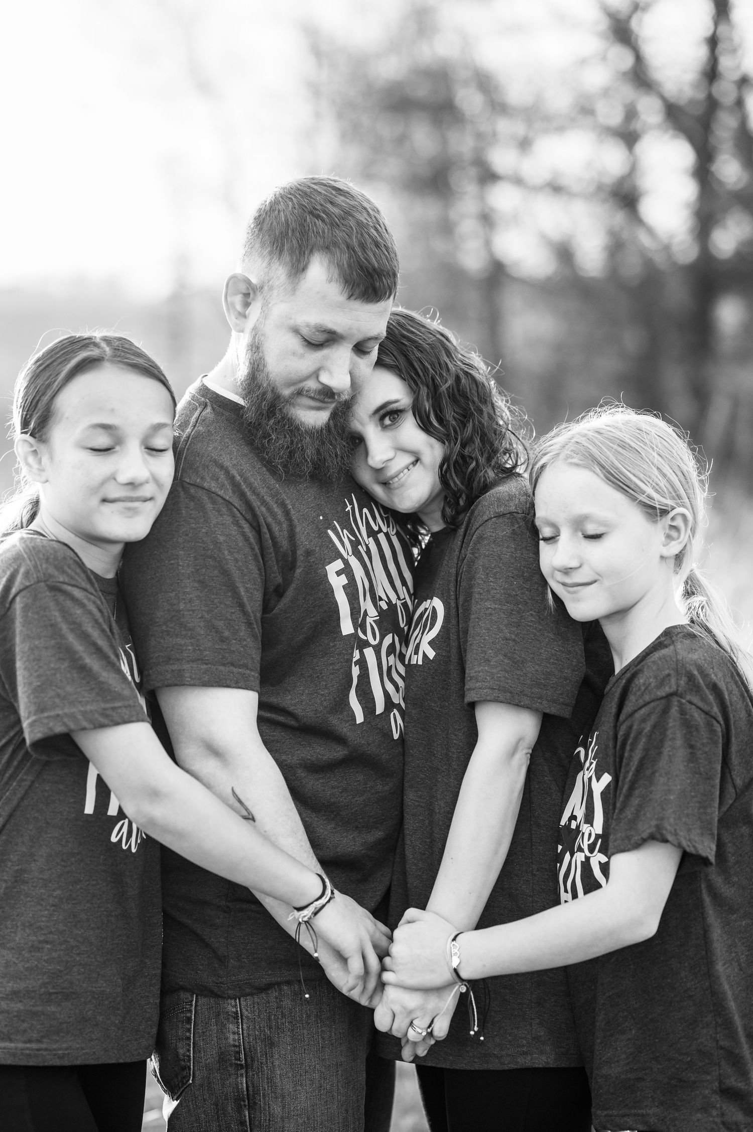 A family wearing matching black t-shirts holds hands in a circle for a touching black and white portrait.