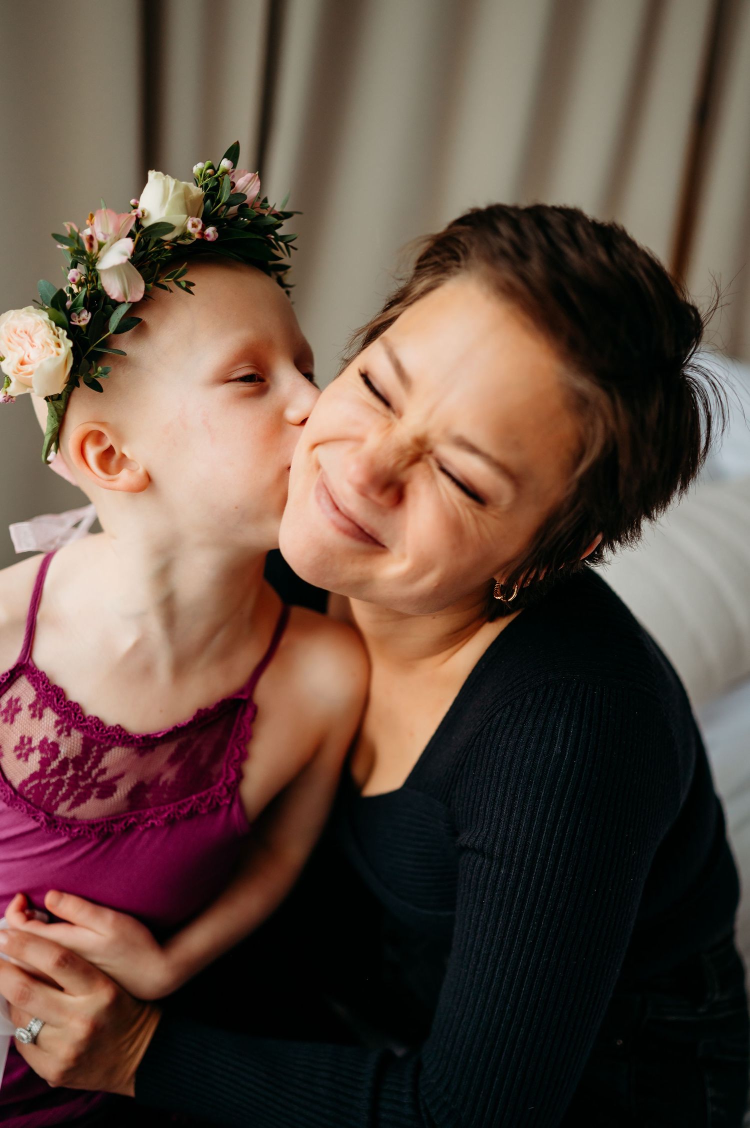 Sweet moment captured of a child wearing a floral crown giving a loving kiss on the cheek.