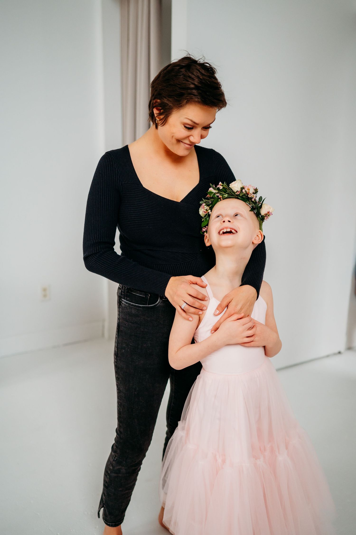 A tender moment captured in a studio as a figure in black interacts with a child wearing a pink tulle dress.
