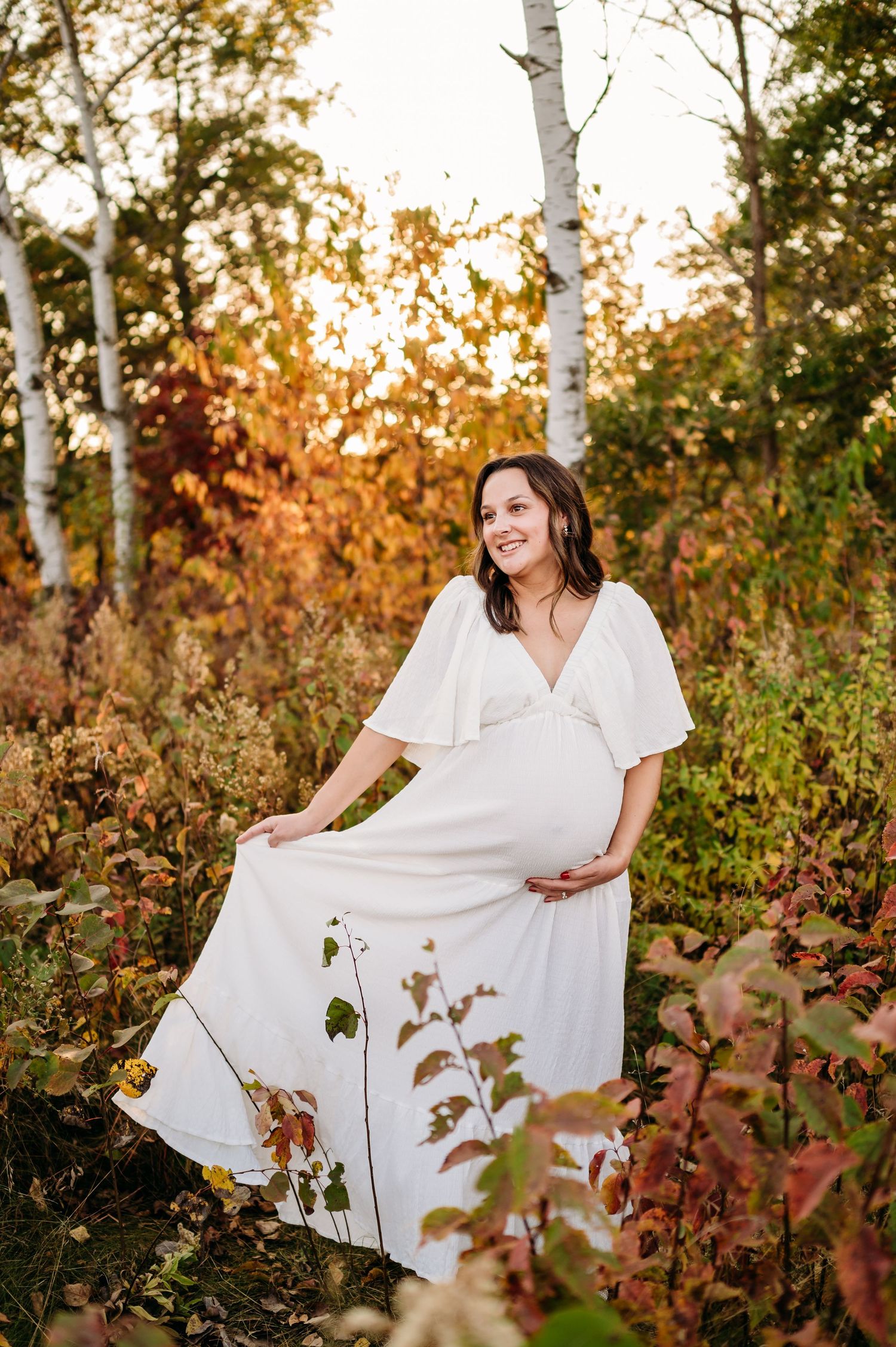 Autumn forest scene with white-dressed figure twirling among birch trees and golden foliage at sunset.