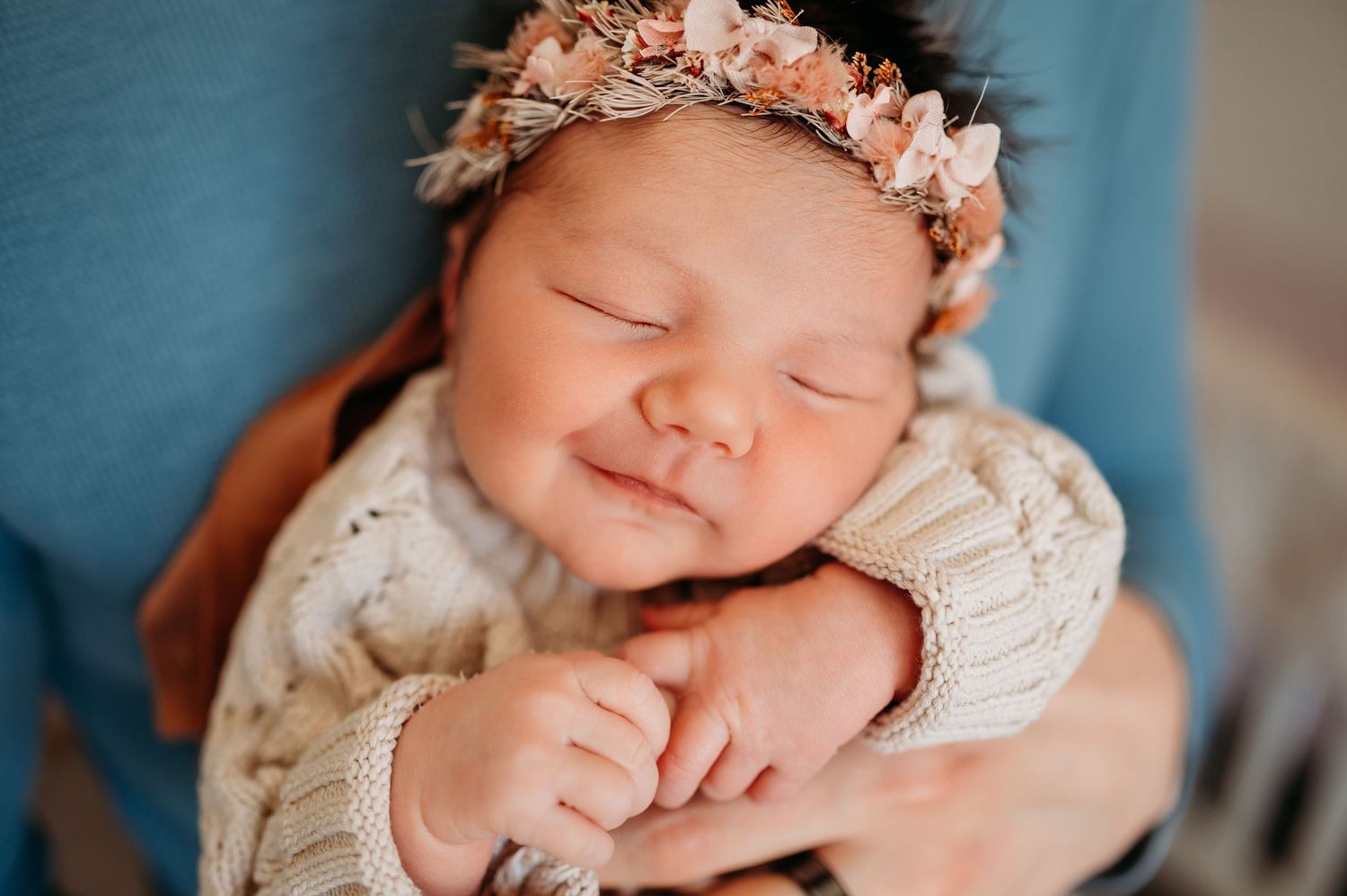 Peaceful sleeping newborn baby wearing soft knitted sweater and delicate pink floral crown.