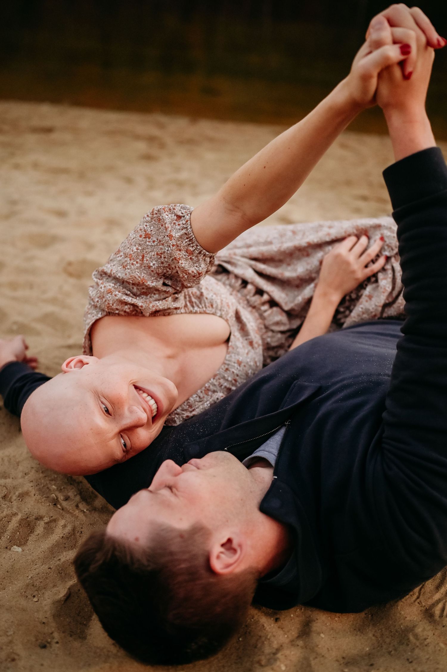 A couple shares a tender moment lying on the beach sand during an autumn day.