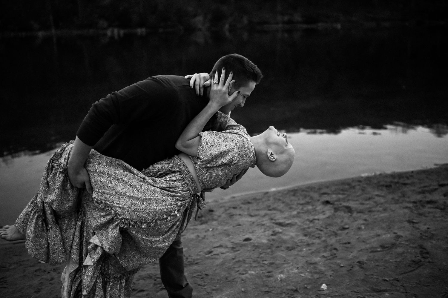 Black and white photo of a couple dancing and twirling on a beach during sunset.