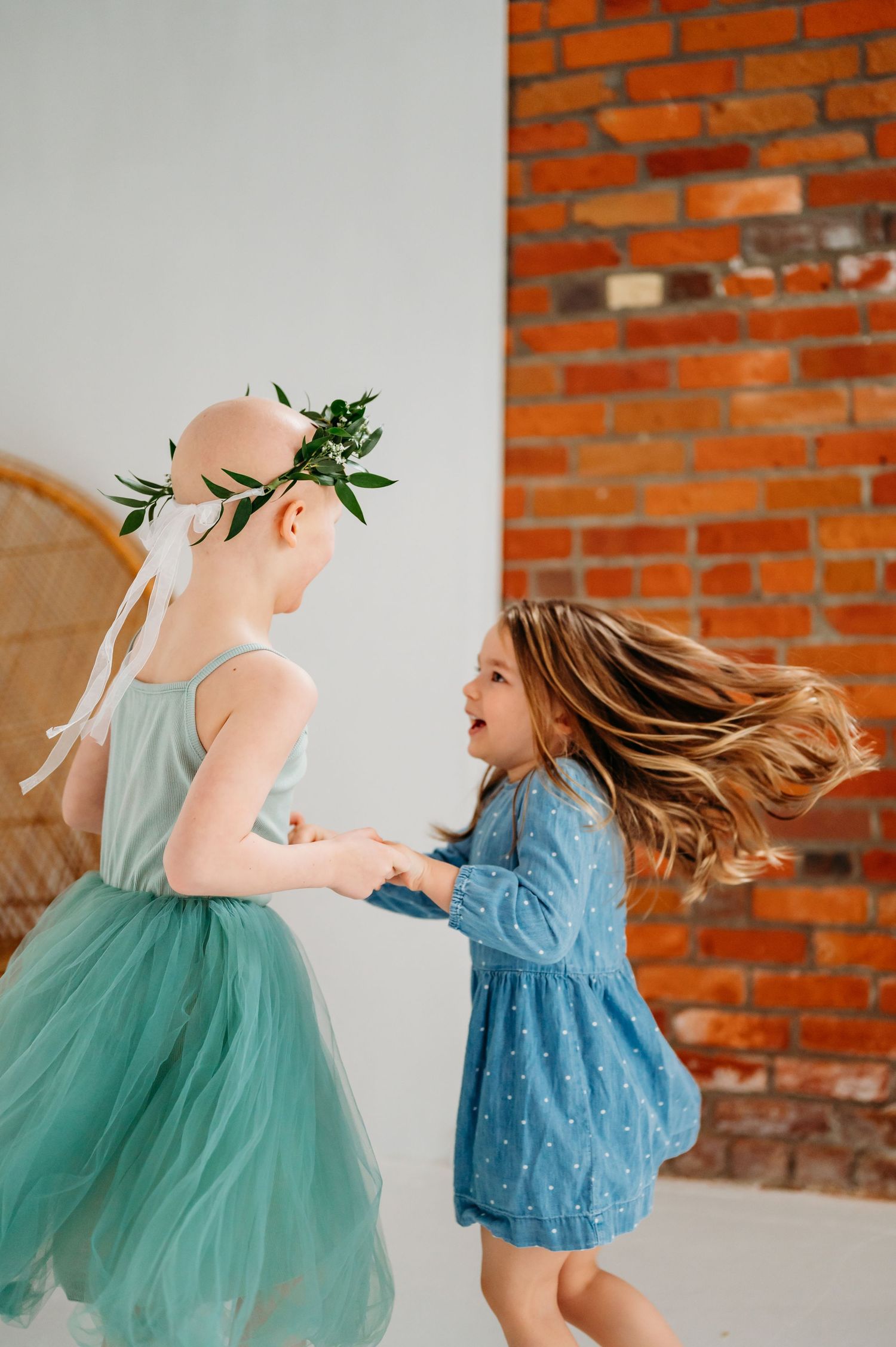 Two children in tulle dresses dancing and playing against a rustic brick wall background.