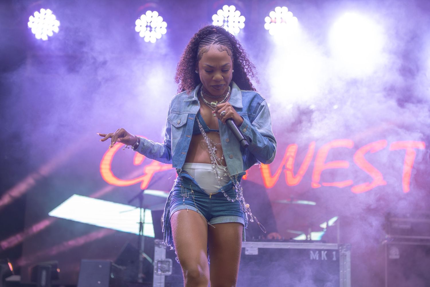 Female performer dancing on stage in denim jacket and shorts at outdoor music festival night.