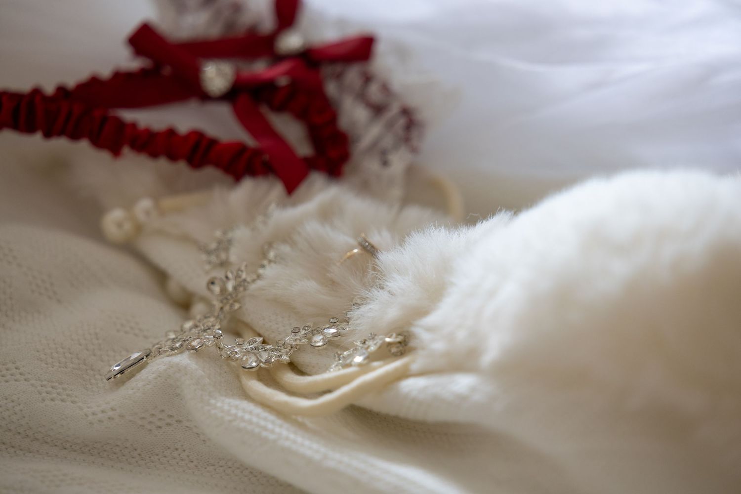 Close-up of elegant wedding accessories including a crystal cross necklace, pearl bracelet, and red ribbon.
