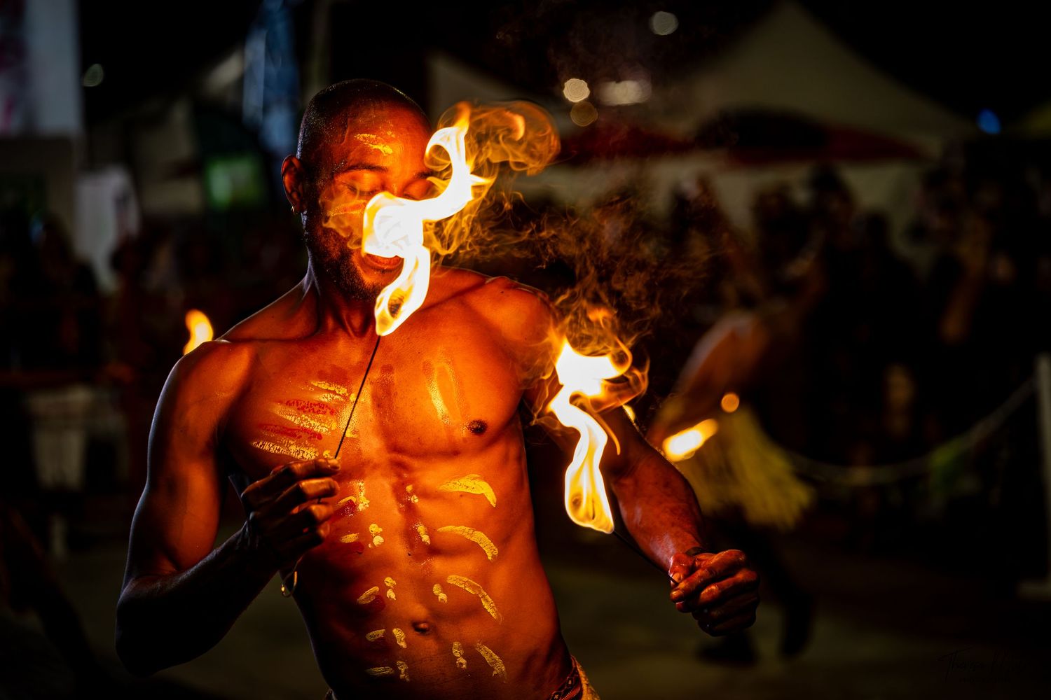 Fire performer breathes flames at a vibrant night festival, showcasing impressive fire dancing skills.