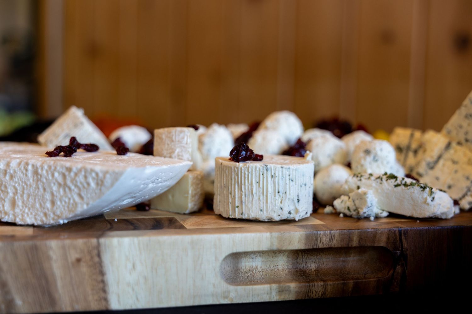Assorted artisan cheeses with cranberry jam displayed on a rustic wooden cutting board.
