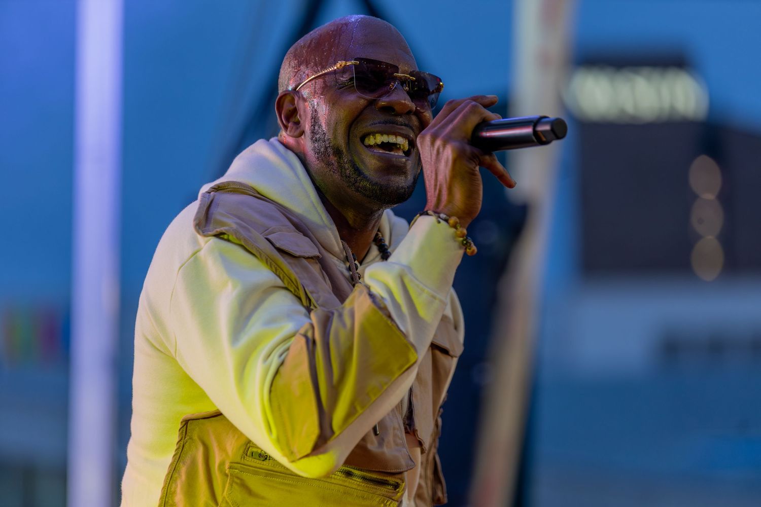 Male singer performing on stage wearing yellow jacket and sunglasses at outdoor music festival.