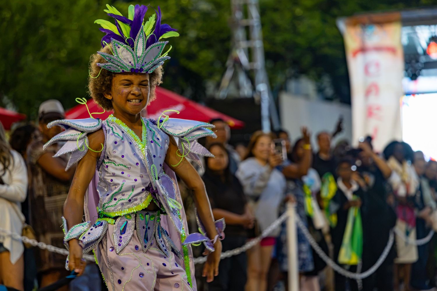 A child in a colorful carnival costume with feathers and decorative wings performs at a festive outdoor cultural parade event.