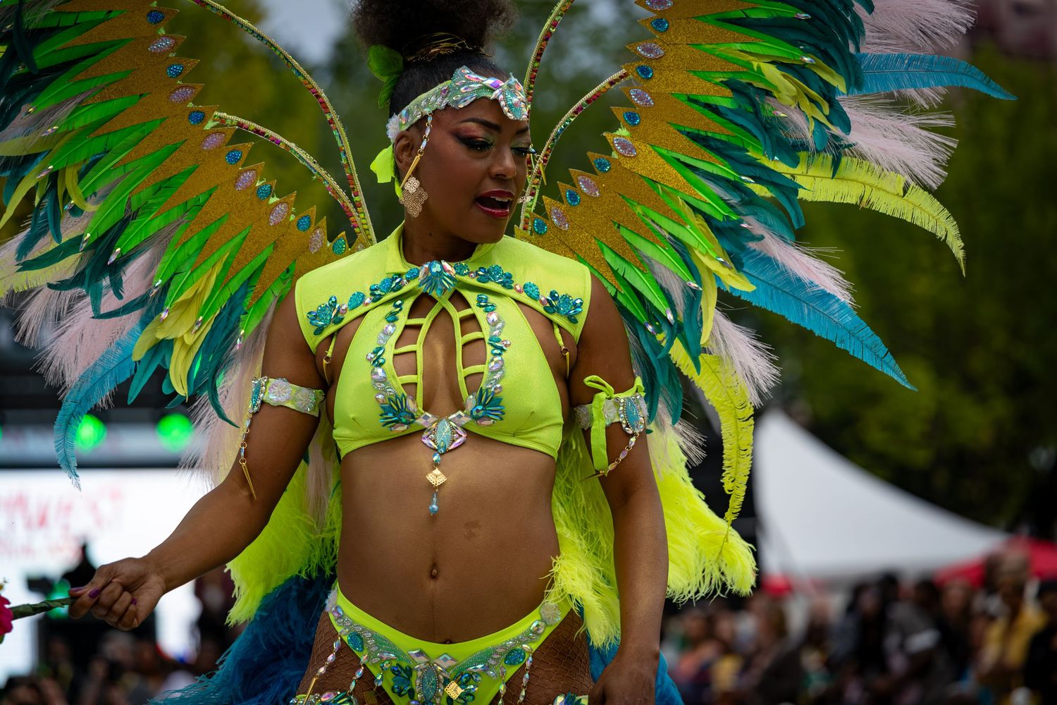 Woman in vibrant green and yellow feathered carnival costume performing at a colorful festival parade.