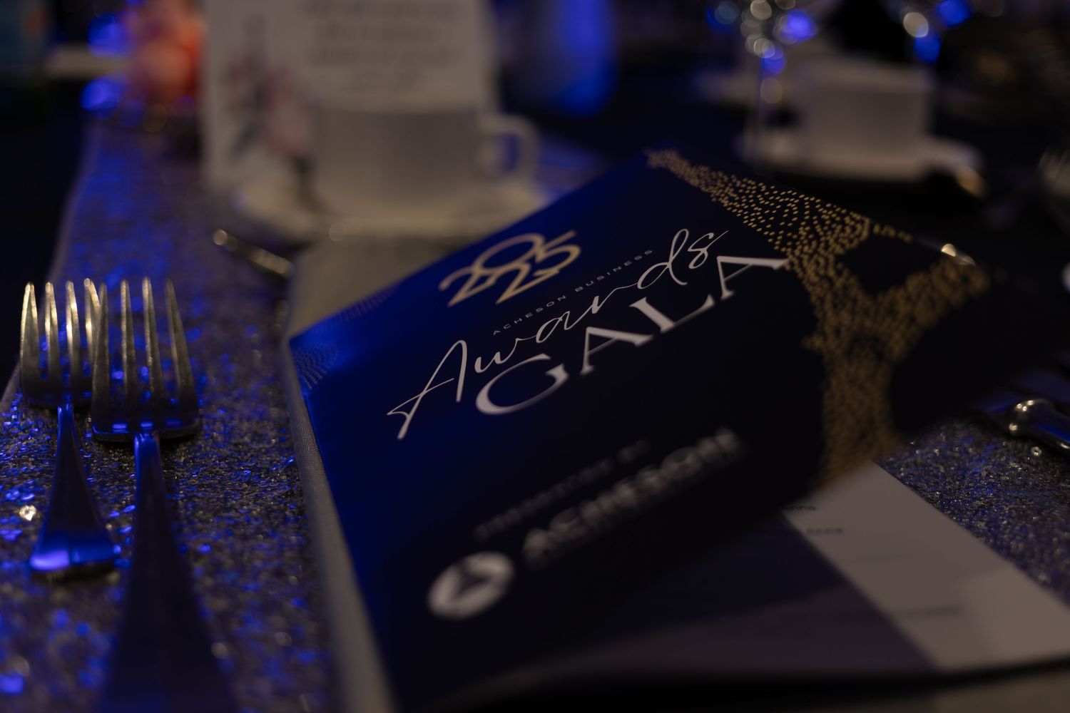 Elegant Awards Gala program booklet on a glittering blue tablecloth with silverware at a formal event dinner.