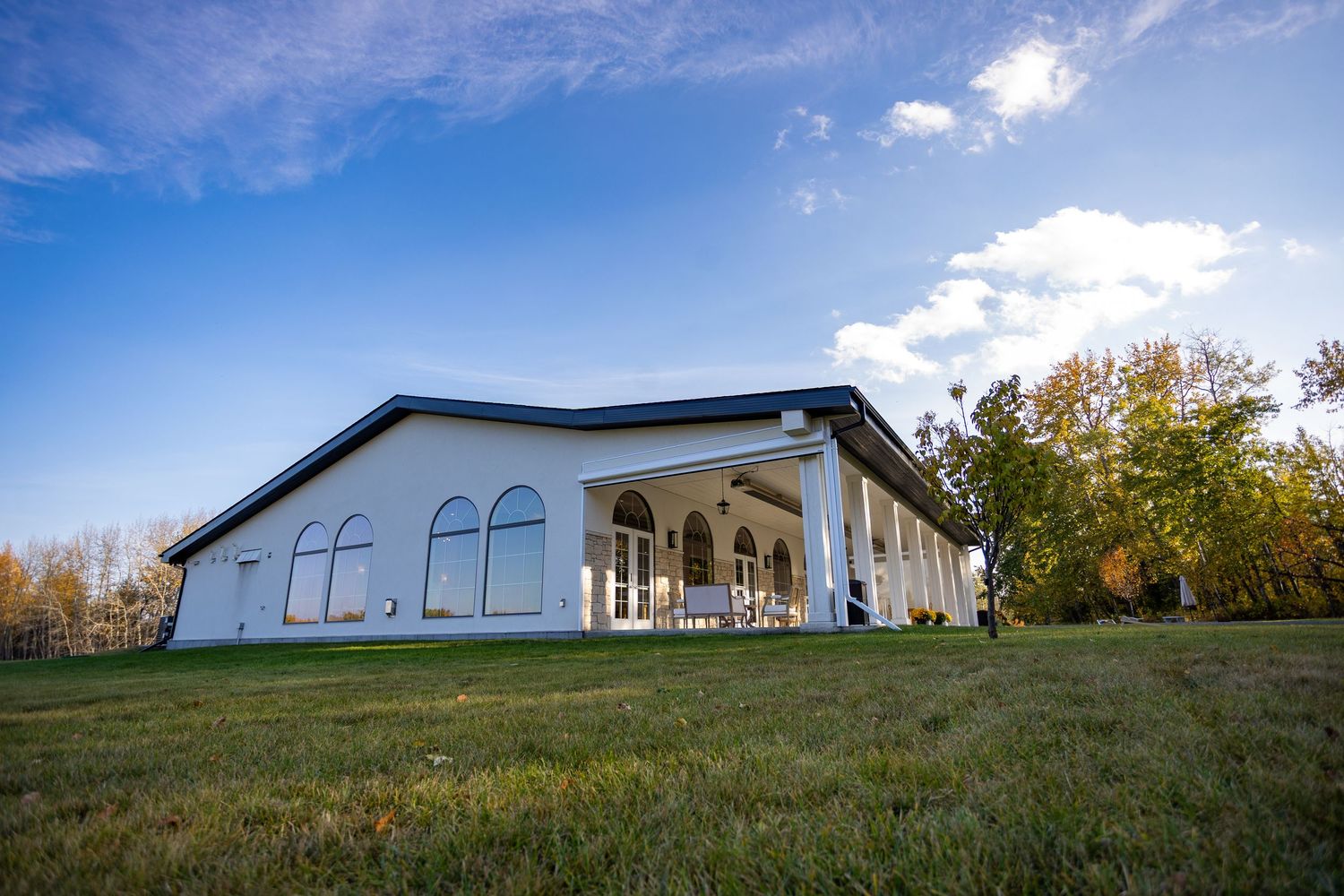 White curved building with arched windows set on a green lawn surrounded by autumn trees.