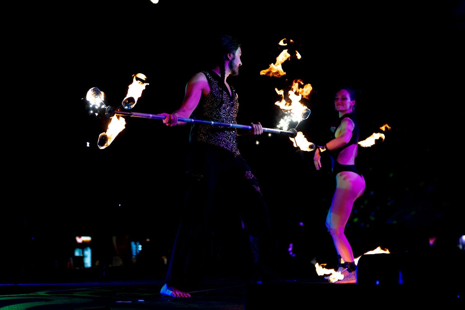 Two performers spinning fire batons in the dark during a dramatic nighttime fire dancing performance.