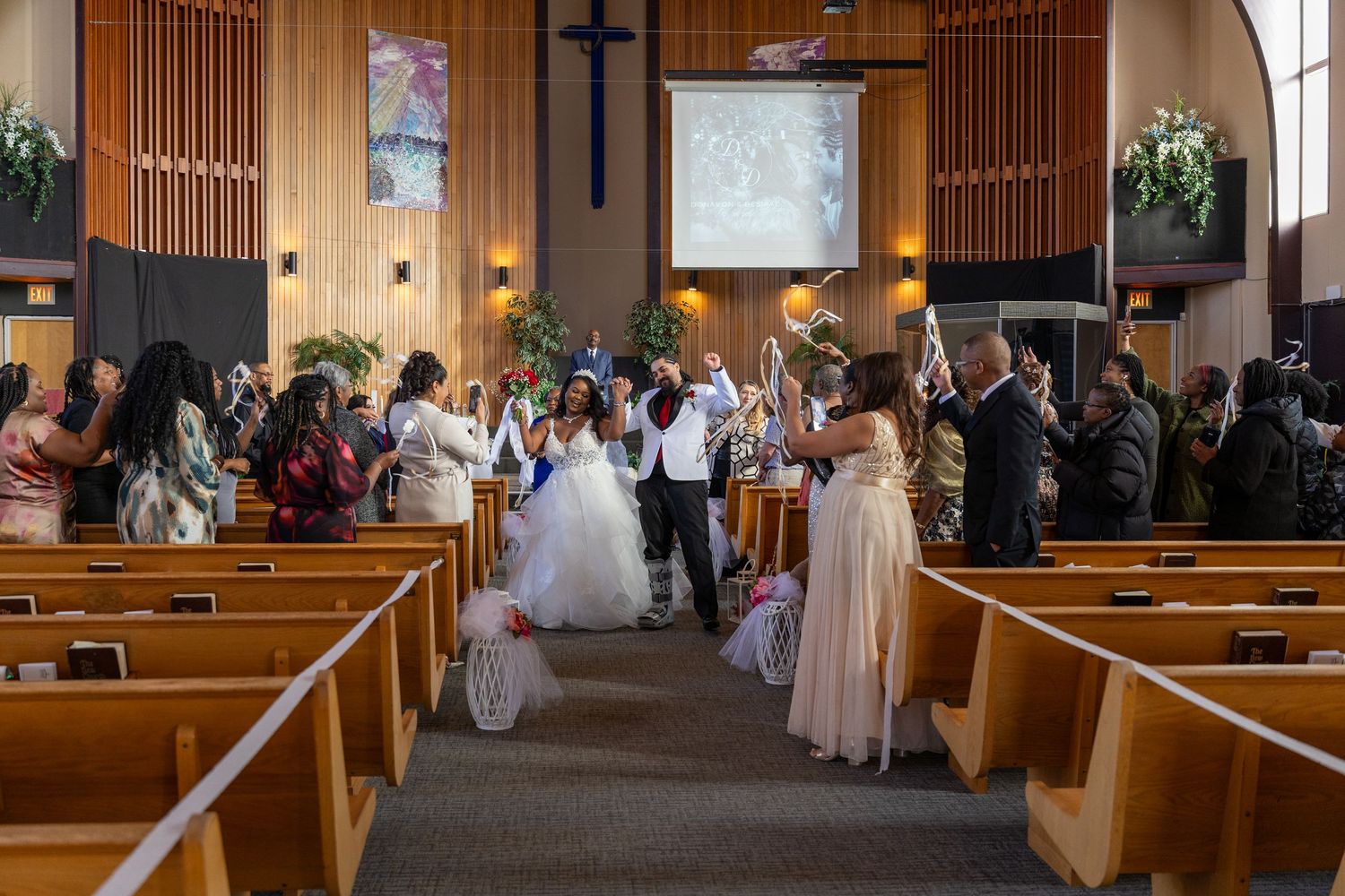 Bride and groom walking down the aisle of a decorated church surrounded by celebrating wedding guests.