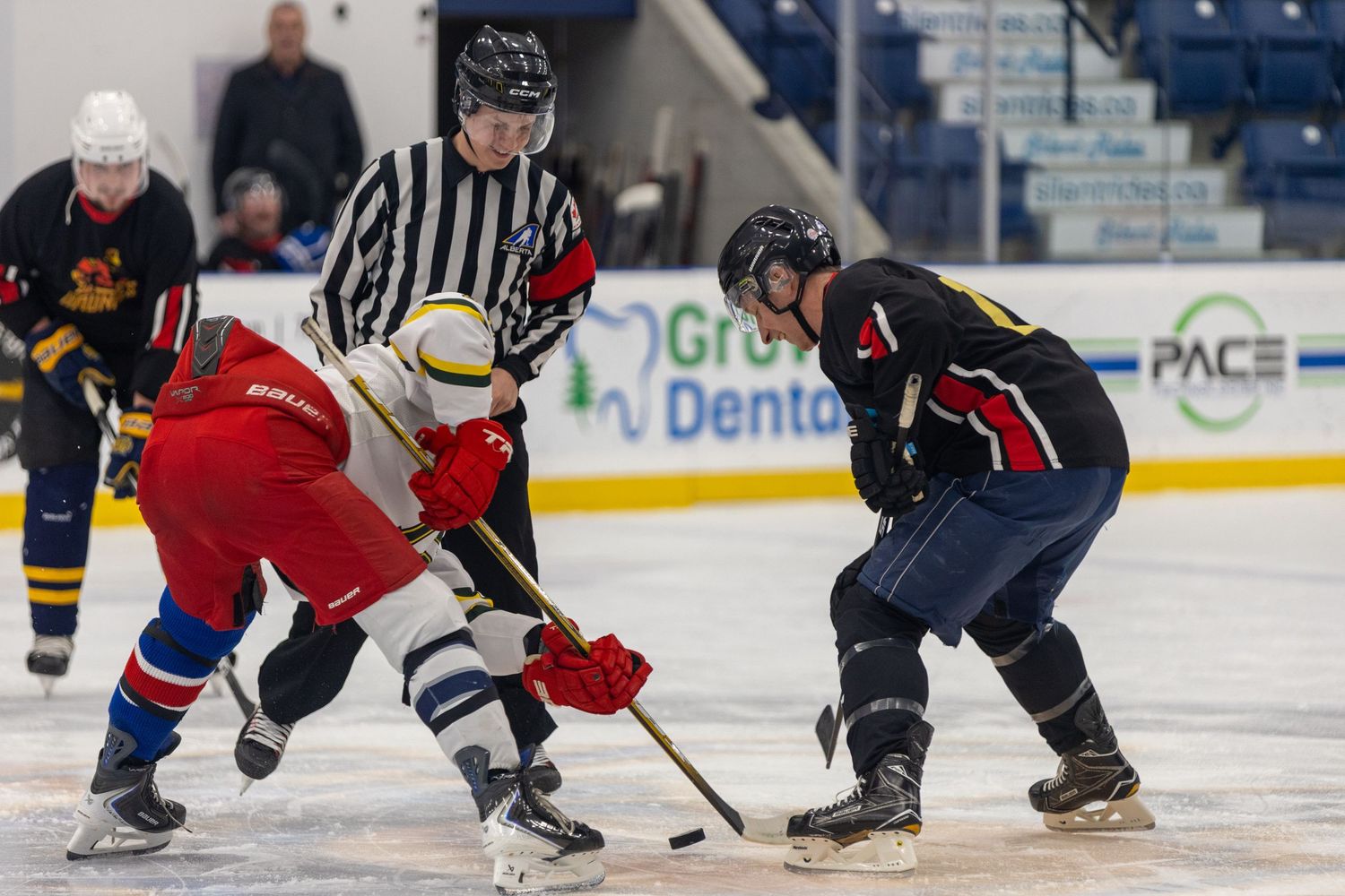 Ice hockey players face off at center ice with a referee dropping the puck during an indoor game.