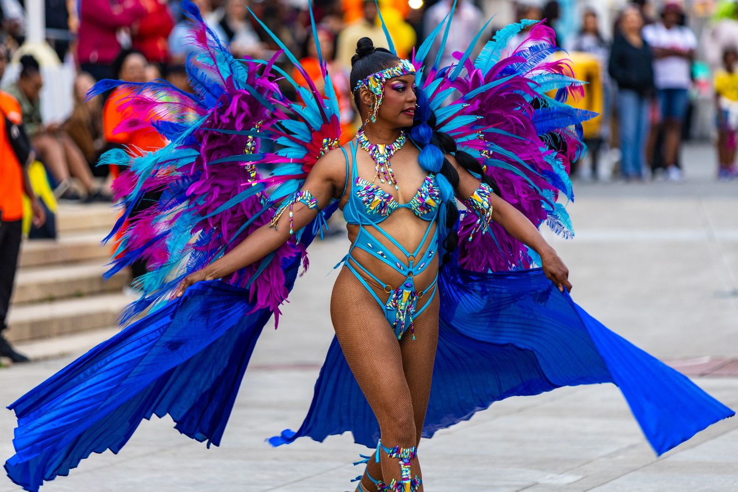 Woman in elaborate blue and purple feathered costume performs at Caribbean carnival parade.