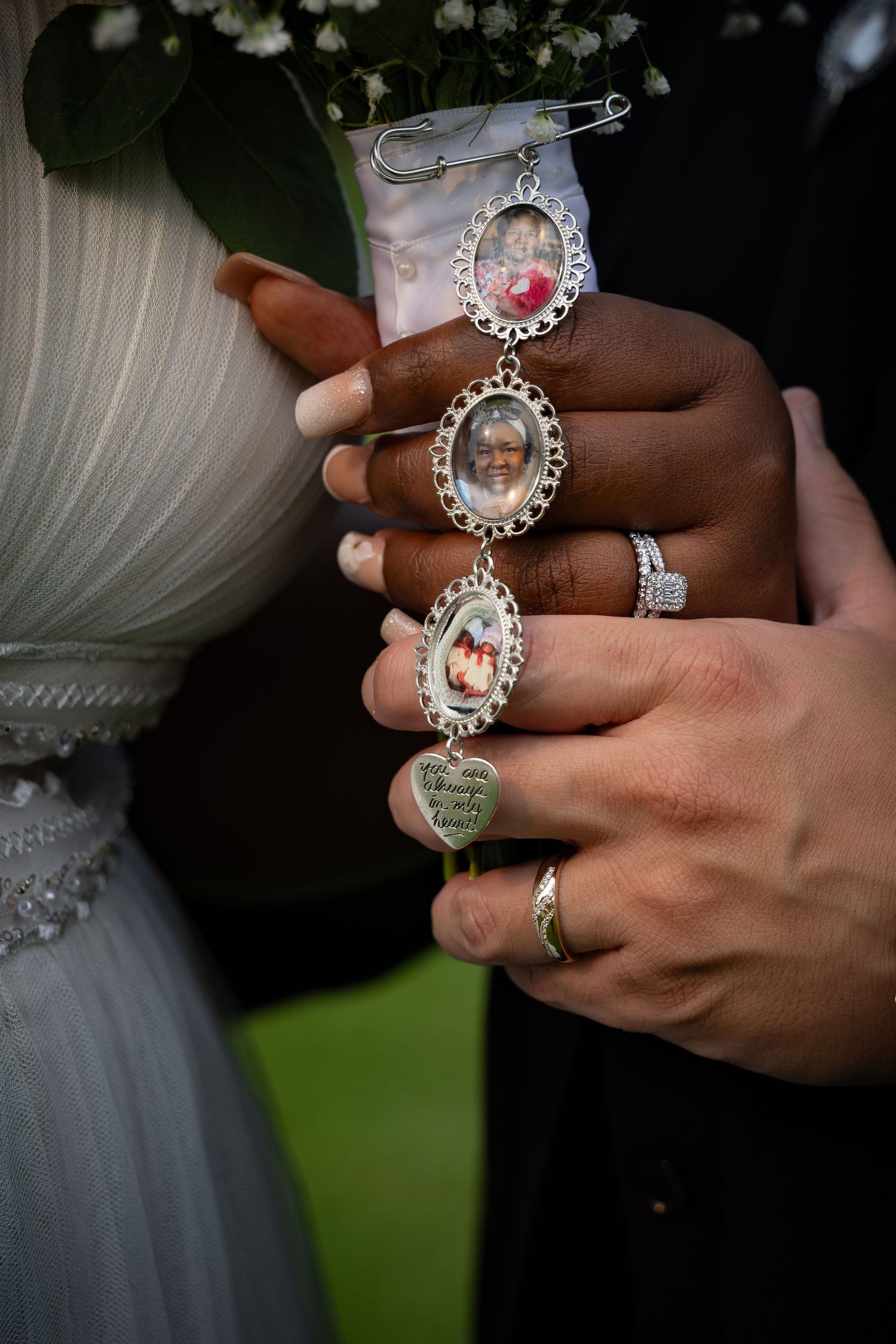 Close-up of interracial couple's hands holding memorial photo charms bouquet brooch at wedding ceremony.