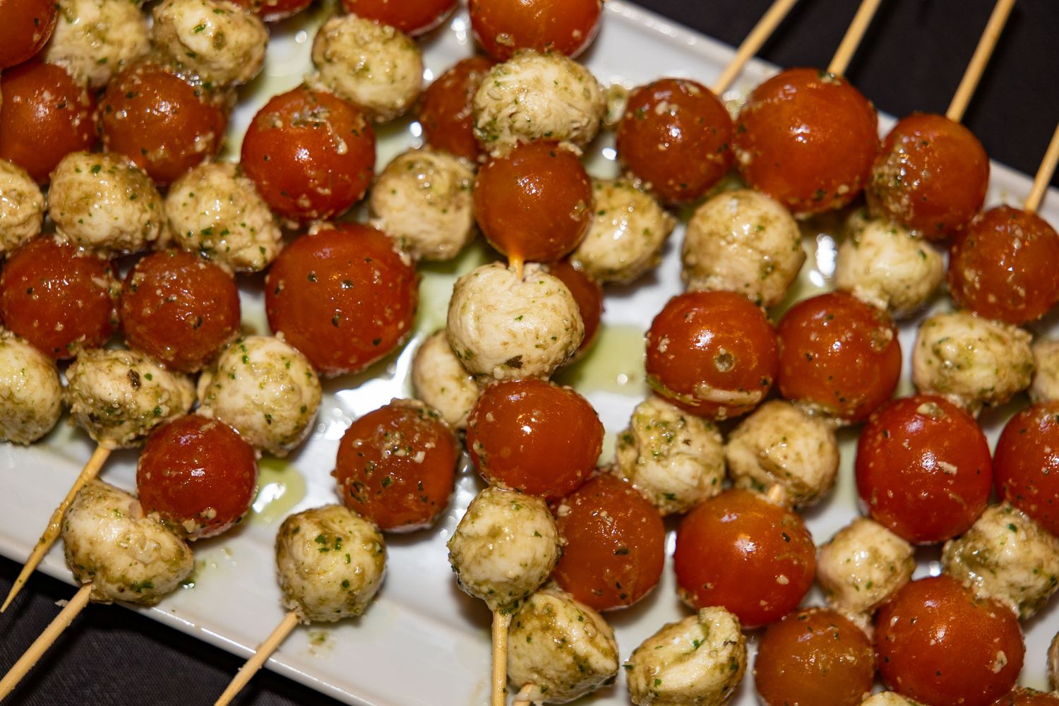 Caprese skewers with fresh mozzarella balls, cherry tomatoes, and pesto sauce arranged on a white platter.