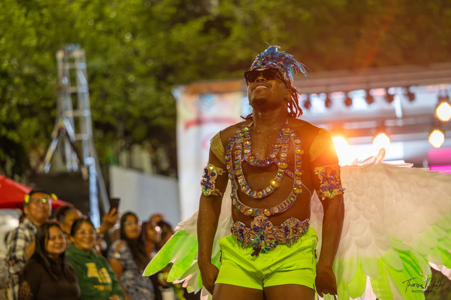 Vibrant carnival performer in neon green costume with feathered headdress dancing at a colorful night festival event.