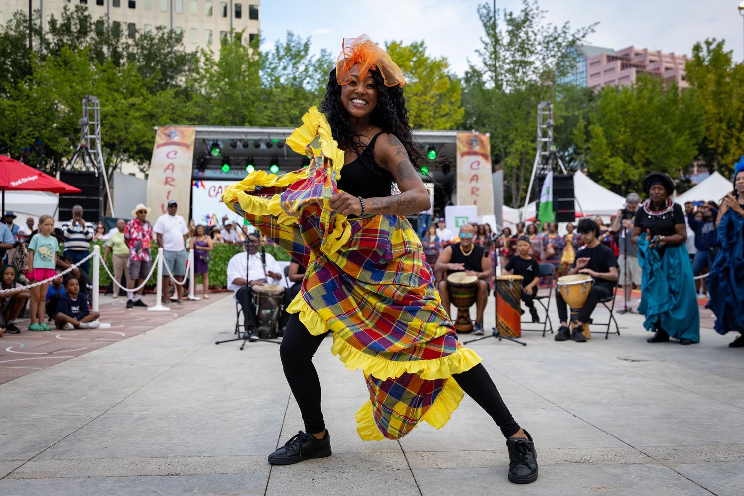 A vibrant dancer in colorful plaid ruffled skirt performs at an outdoor cultural festival stage.