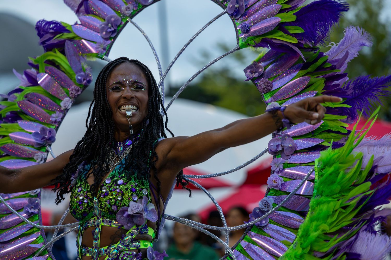 Woman in vibrant purple and green carnival costume with feathered headdress dancing at outdoor festival.