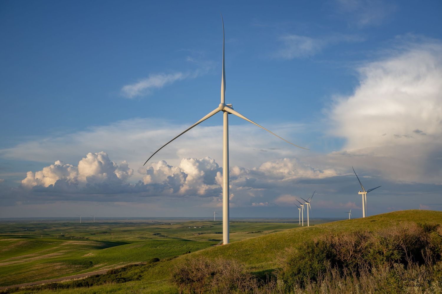 Wind turbines on rolling green hills under dramatic cloudy sky in open prairie landscape.