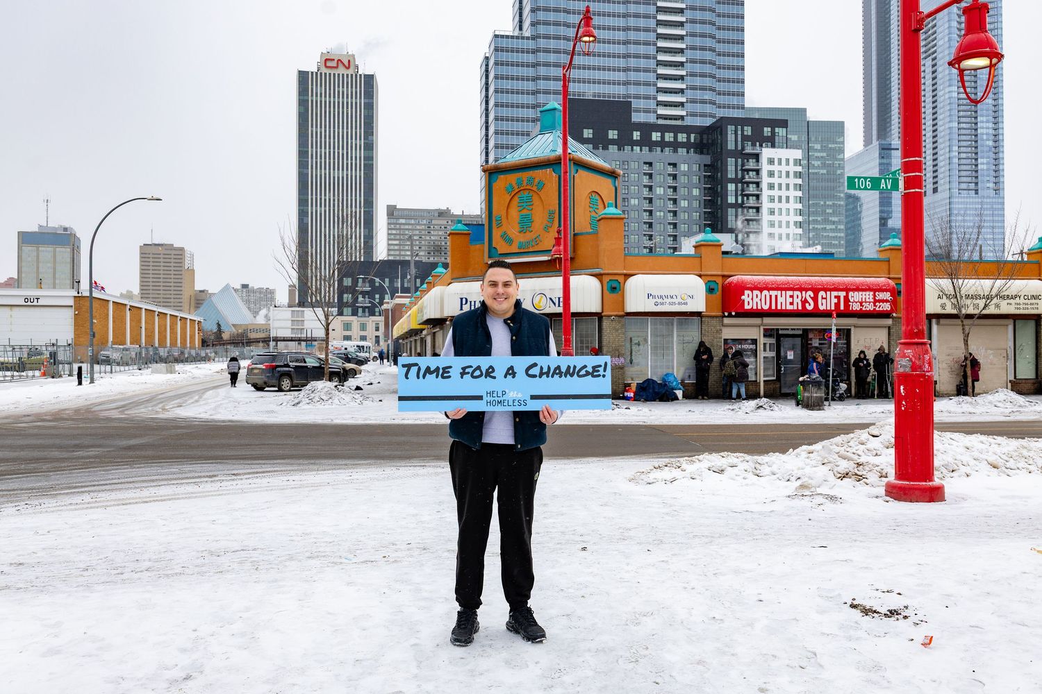 Man holding 'Time For A Change' sign in snowy urban setting with city skyline in background.
