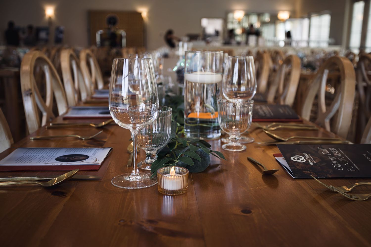 Elegant rustic wooden dining table set with wine glasses, candles, and greenery for a formal dinner event.
