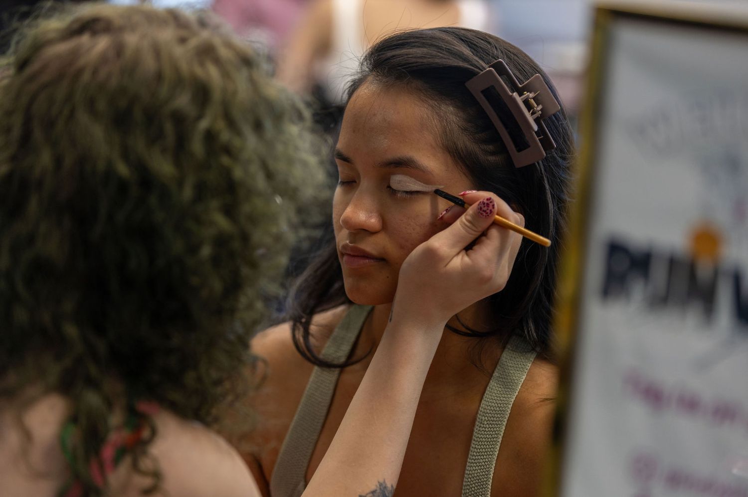 Young Asian woman having eye makeup professionally applied with brush at beauty event.