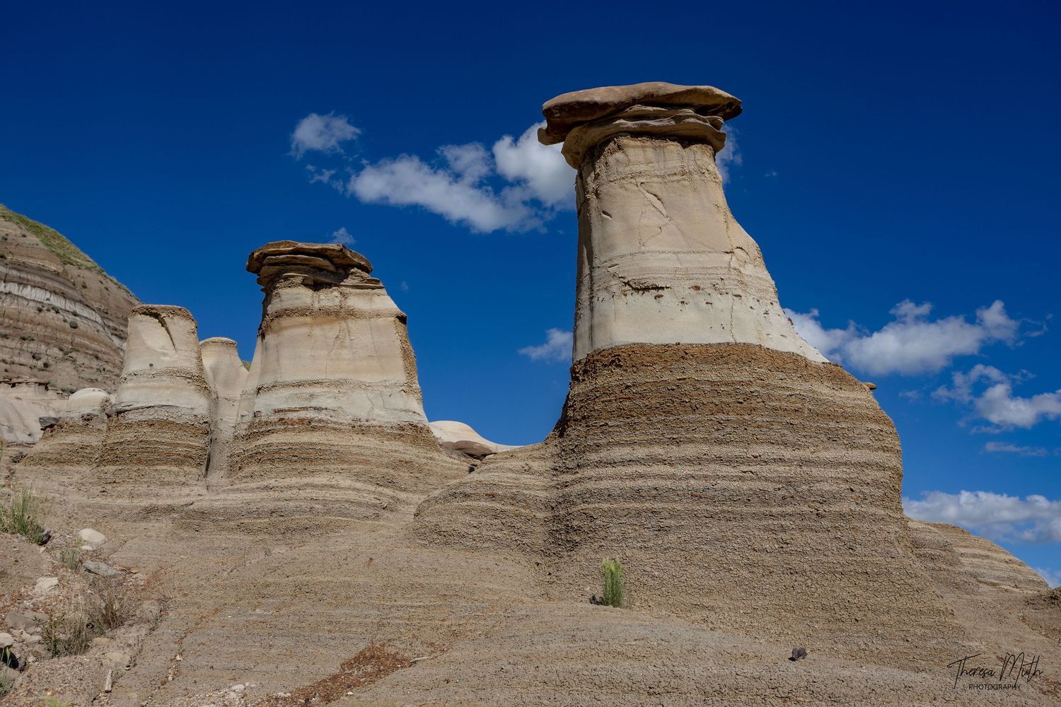 Two towering hoodoo rock formations rise against a vivid blue sky in the Canadian Badlands, Alberta.