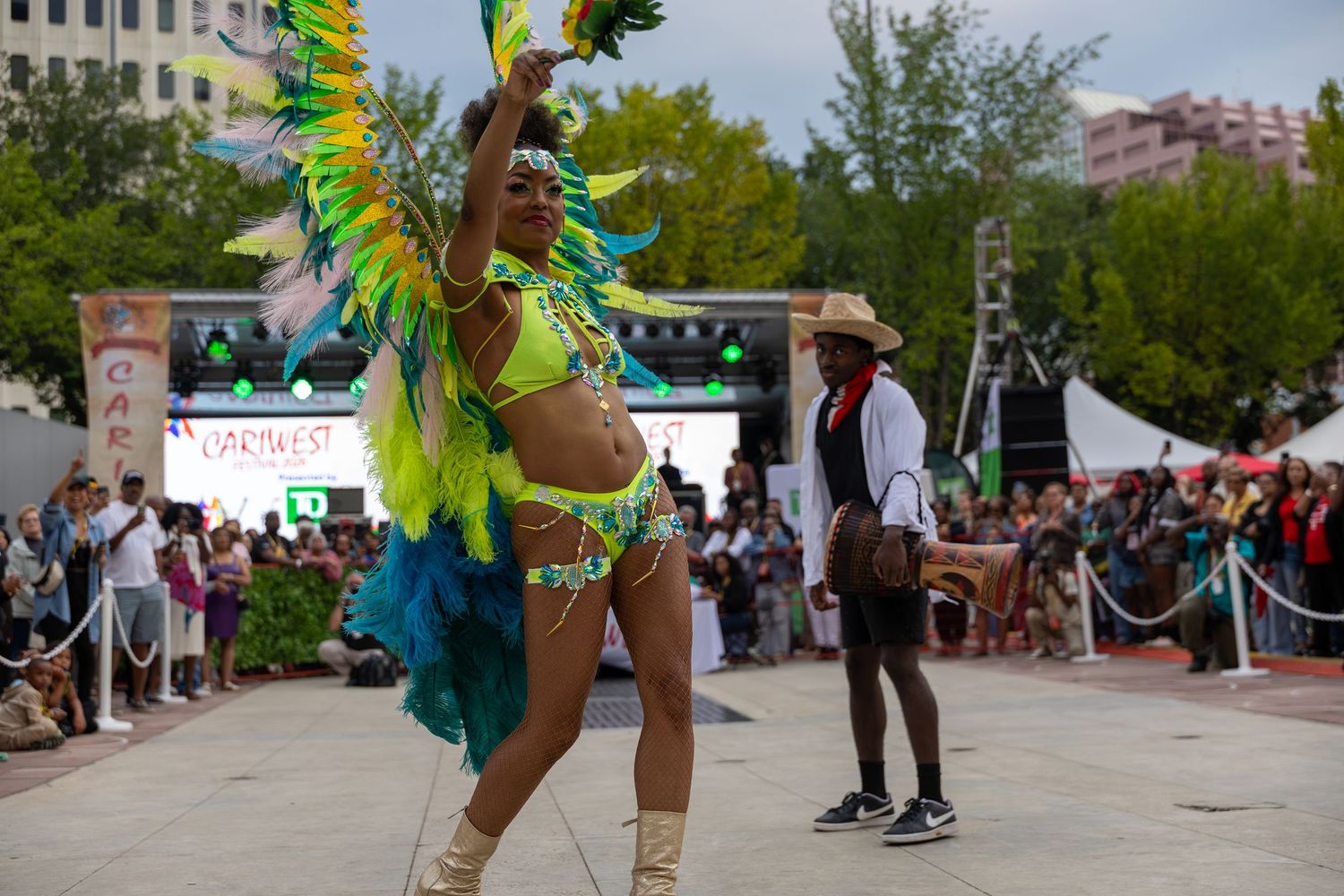 Vibrant carnival dancer in colorful feathered costume performs on outdoor stage at festive cultural event.