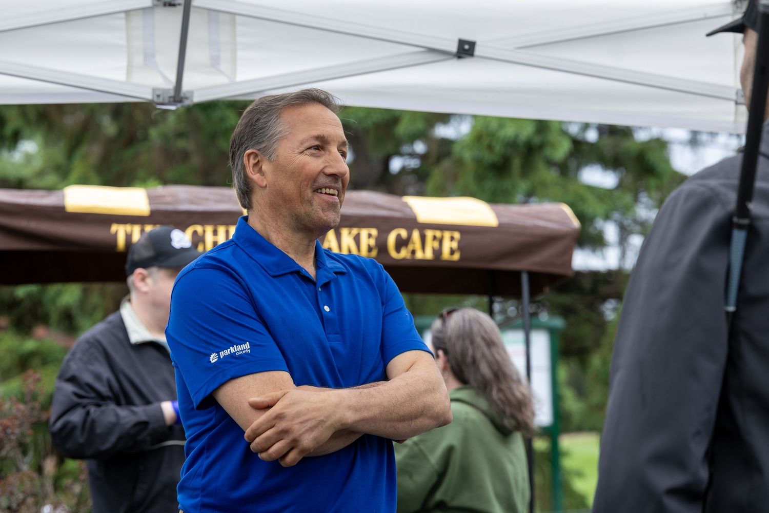 Man in blue polo shirt smiling with arms crossed at outdoor cafe event.