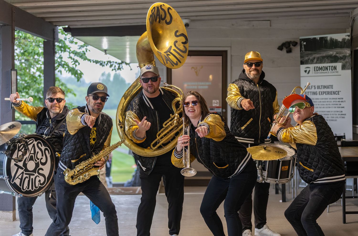 Energetic brass band poses with instruments in black and gold jackets outside Edmonton venue.