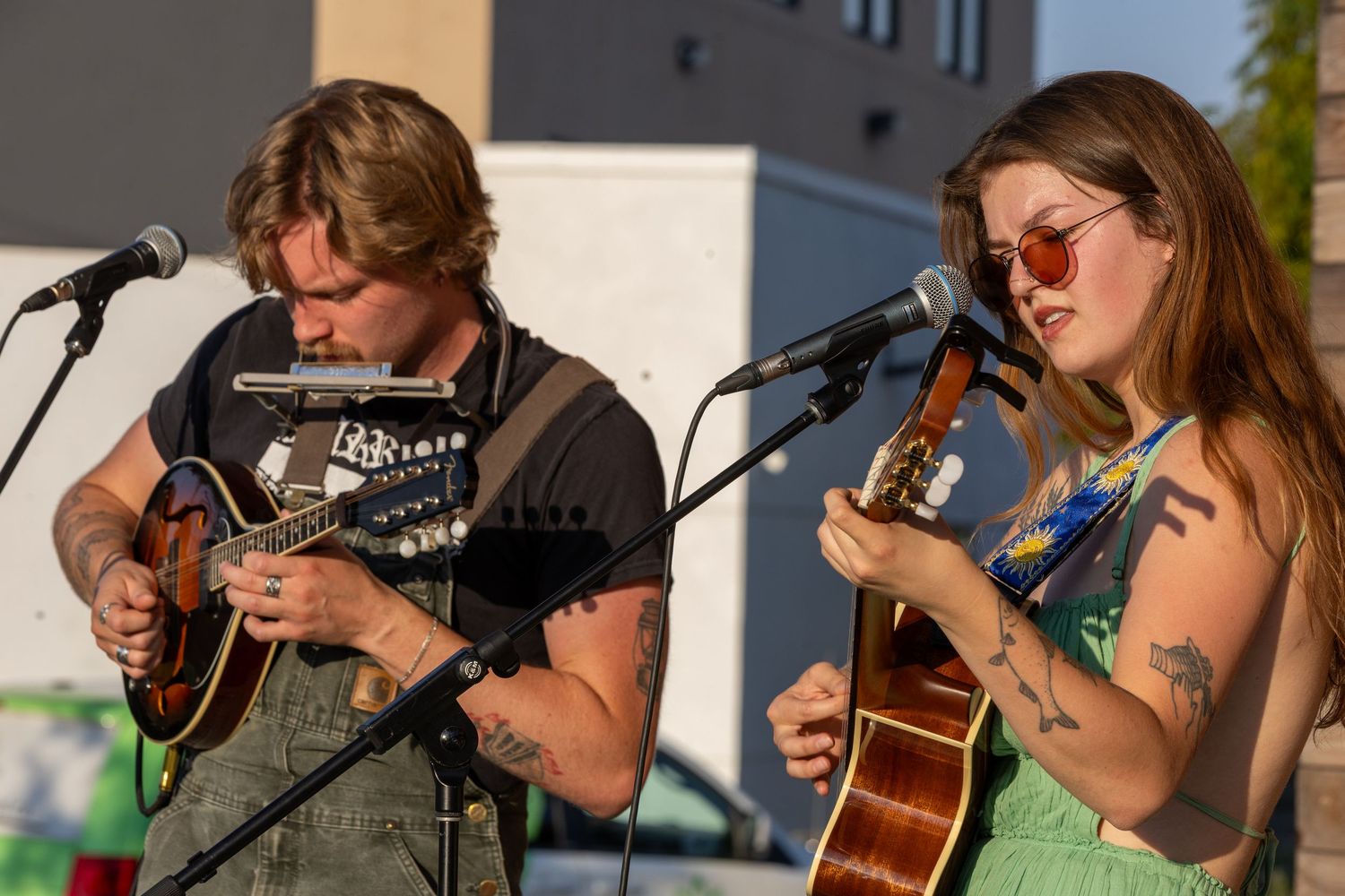 Man and woman play mandolin and guitar together at outdoor music performance at dusk.