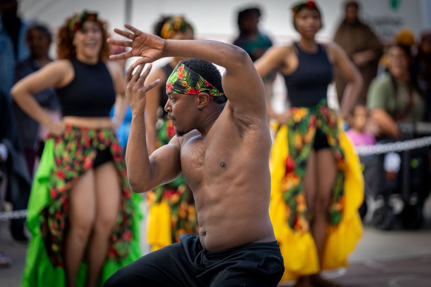 Shirtless male dancer performs African dance wearing colorful headband at outdoor festival.