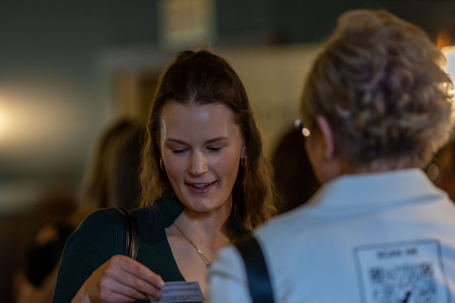 Smiling young woman in green top socializing at an indoor networking event.