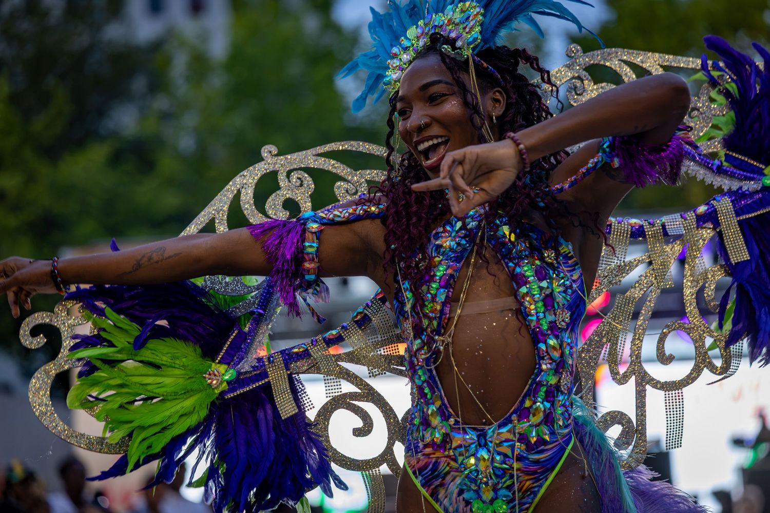 A woman in a vibrant feathered carnival costume dances joyfully during a colorful street parade festival.
